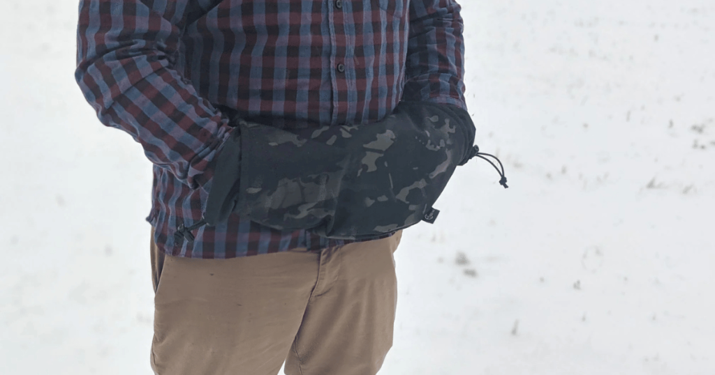 A man standing in the snow using a Cole-TAC Hand Hut to keep his hands warm.