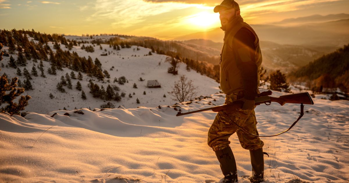 A man on a cold weather hunt standing on a snowy mountain.