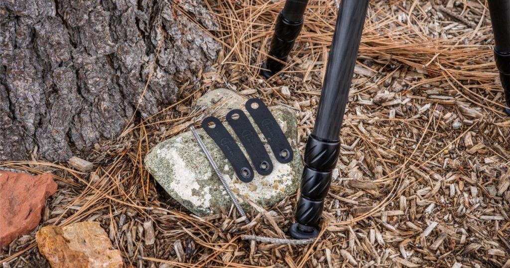 Three black Cole-TAC Tripod Staking Straps on a rock next to a tripod.