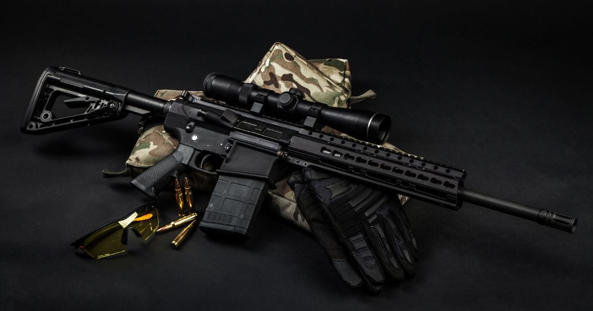 A carbine resting on top of several shooting bags with rifle rounds laying nearby.