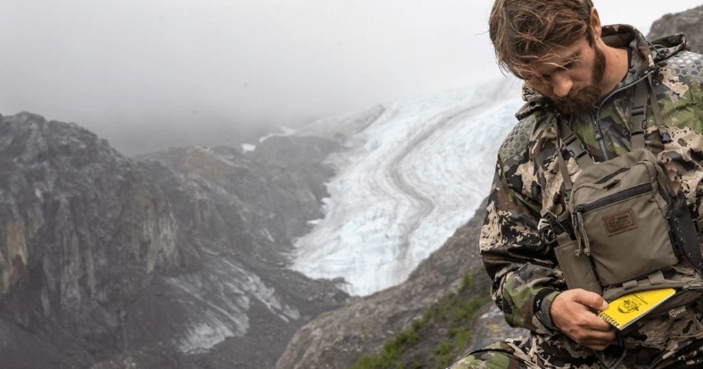 A man standing in the mountains looking at a Cole-TAC dope card.