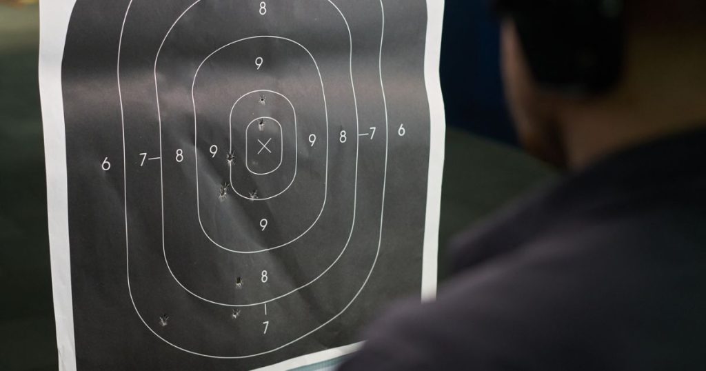 A person at a shooting range looking at their paper target.