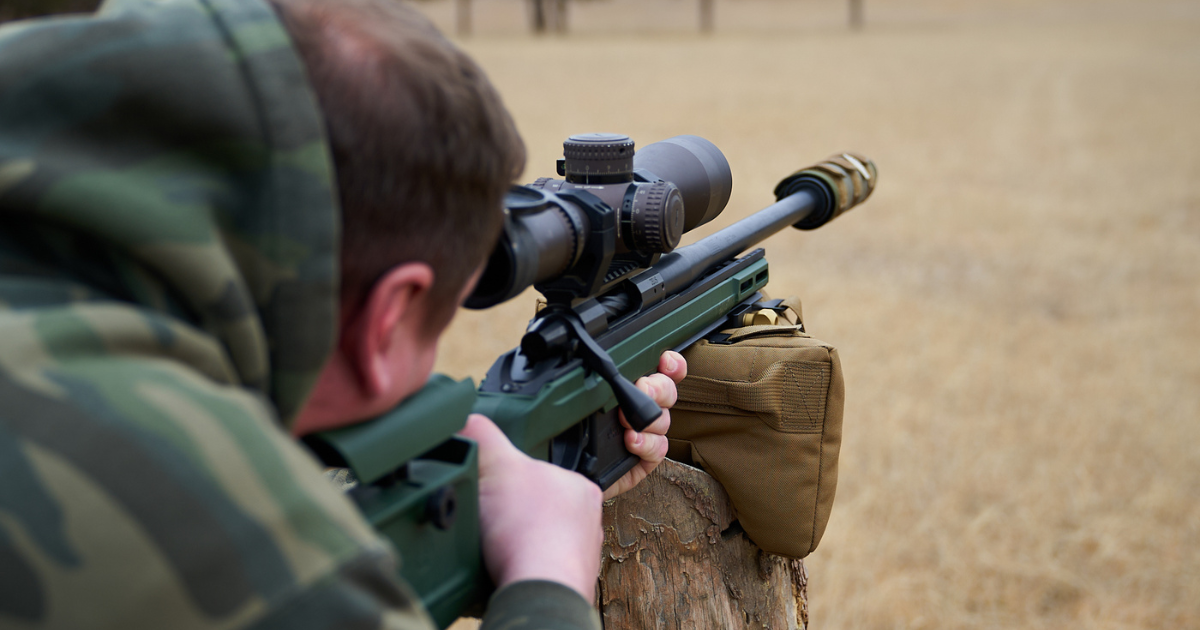 A man lining up his shot with his long range rifle using a Cole-TAC suppressor cover and shooting bag.