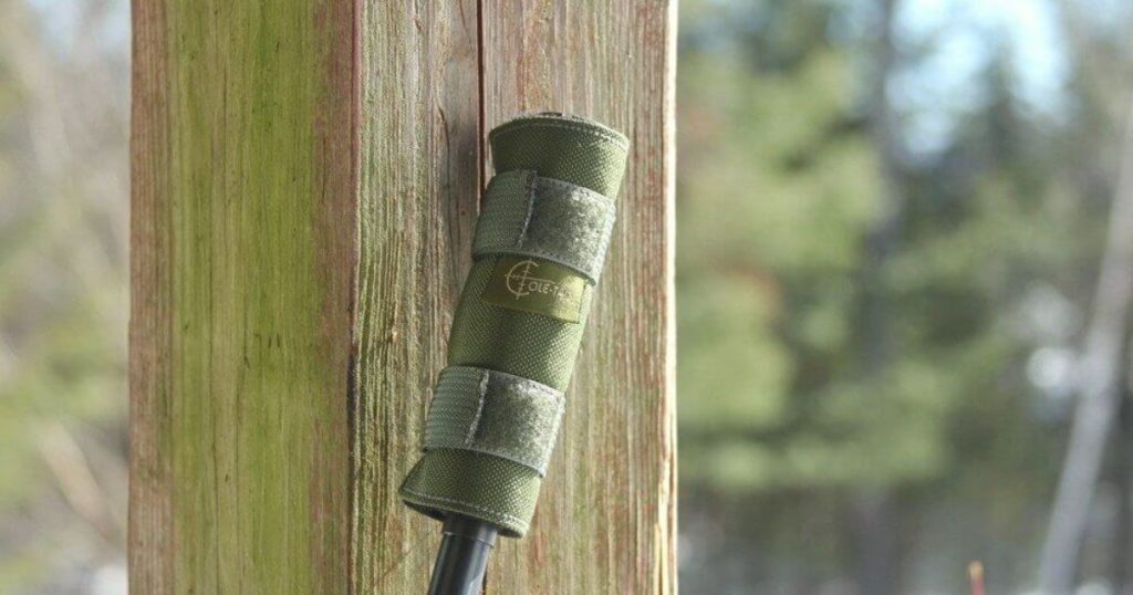 A suppressor with a Cole-TAC suppressor cover on a rifle leaning against a wooden pillar.