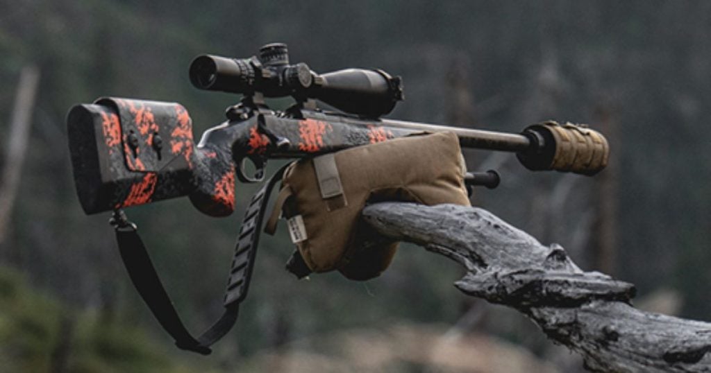 A rifle on a shooting bag on a branch with a suppressor cover.