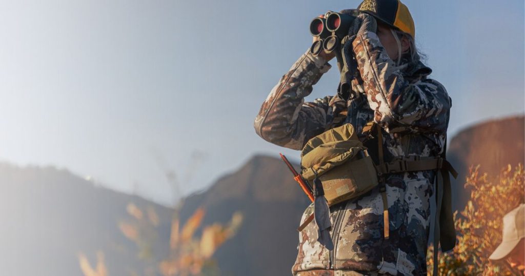 A woman hunter looking through binoculars wearing a bino harness from Cole-TAC.