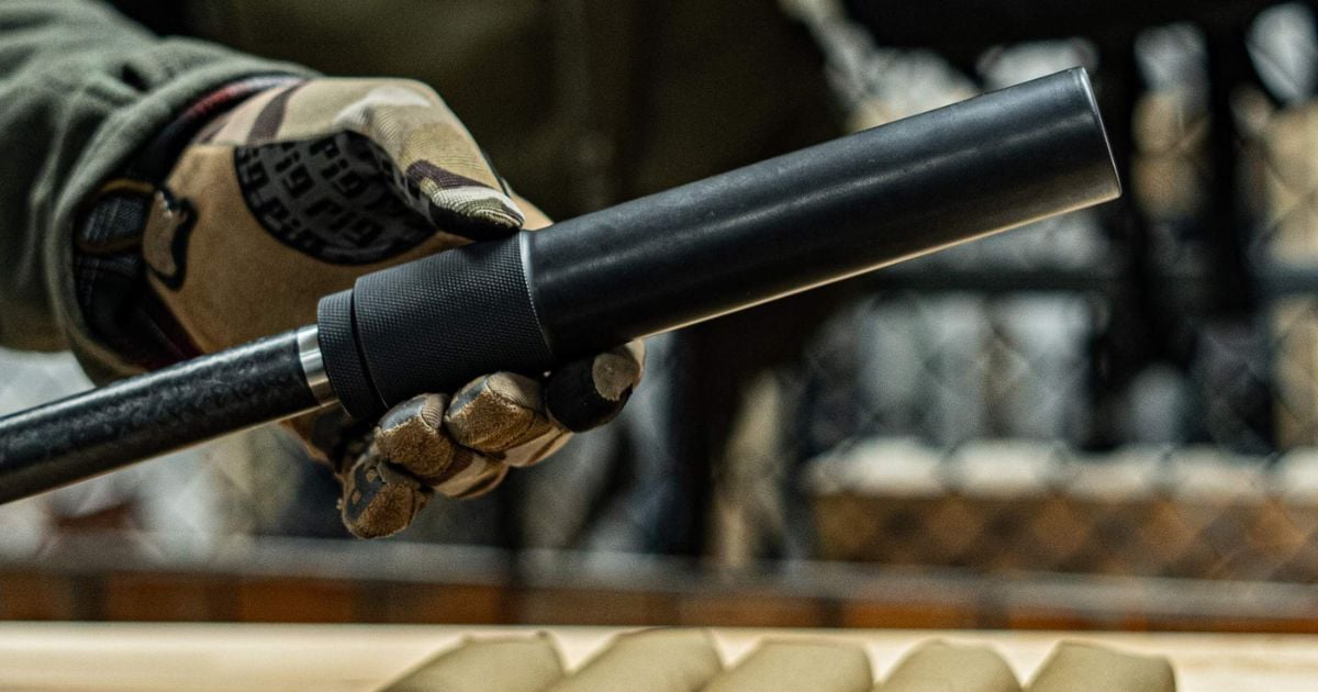 A person taking a cooled down suppressor off his rifle.