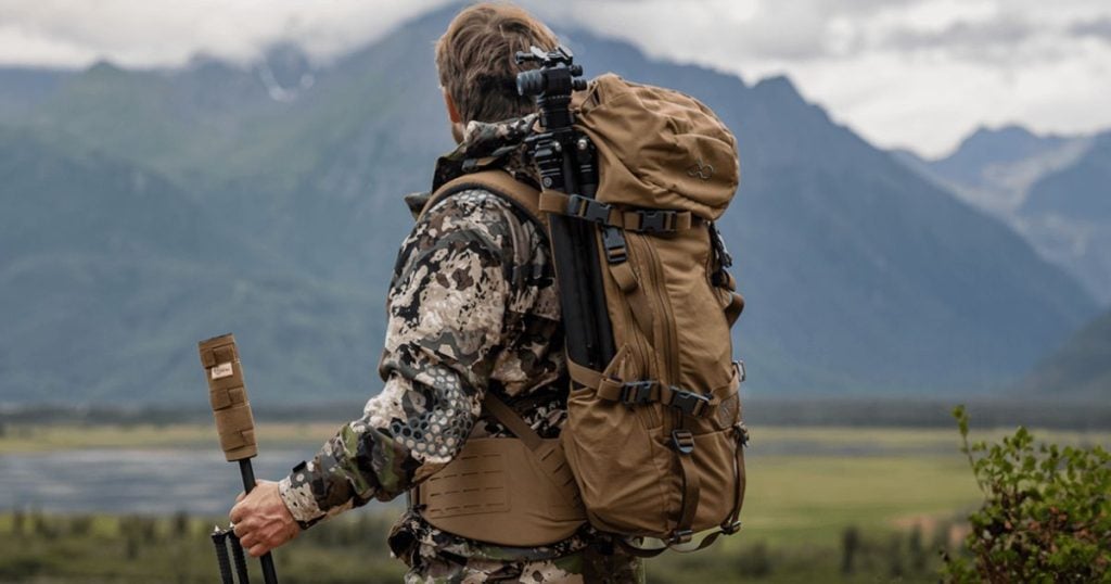 A man out hunting carrying a pack and rifle with a suppressor and suppressover cover by Cole-TAC.