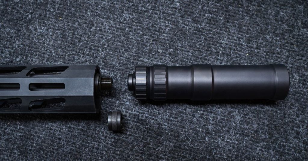 A black suppressor on a gray background near a gun.