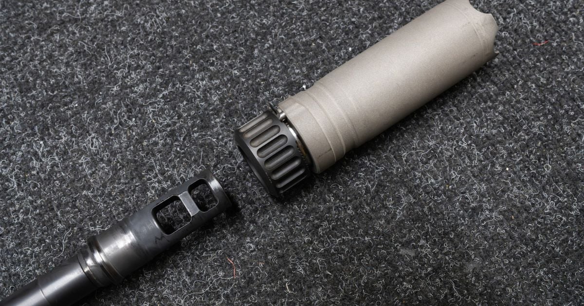 A gray suppressor near a gun on a light gray background.