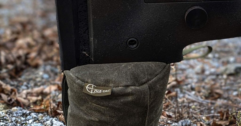 The butt of a hunting rifle sitting on top of a Cole-TAC shooting support bag.