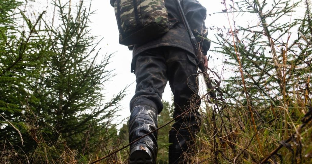 A man walks a long a trail carrying his western hunting gear.